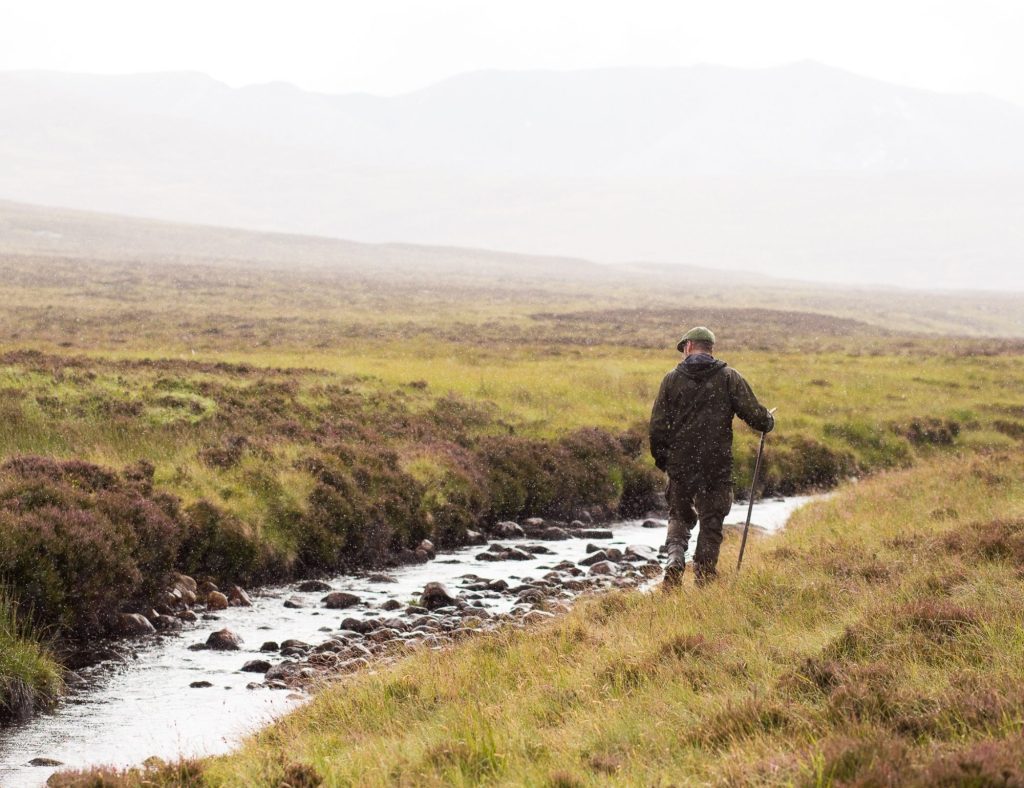 A man walking alongside a stream with misty mountains in the background