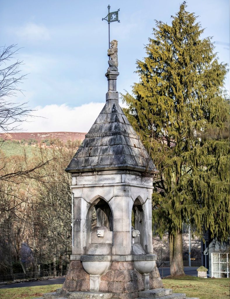 A historic spire landmark in the village of Braemar with a tree and blue sky