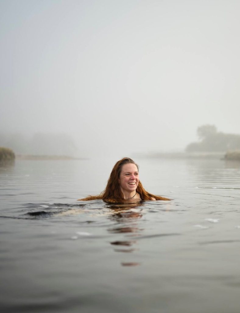 Annie Armstrong, wild swimming guide, in the water with mist in the background.