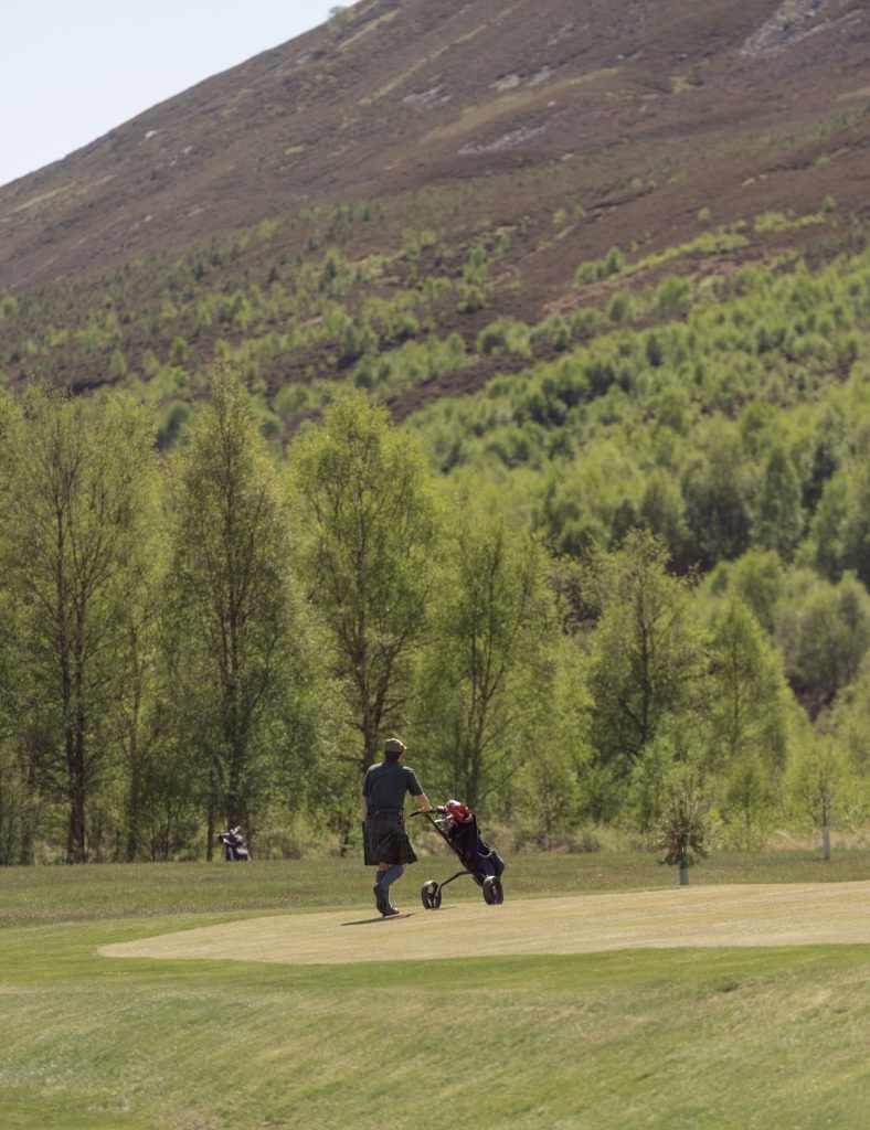 Golfer playing at Braemar golf club wearing a kilt with landscape in the background.