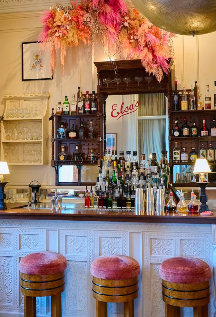 Elsa's cocktail bar, with three pink bar stools and bottles behind the bar