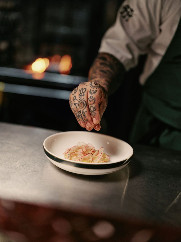 A chef with a tattooed hand putting finishing touches to a dish