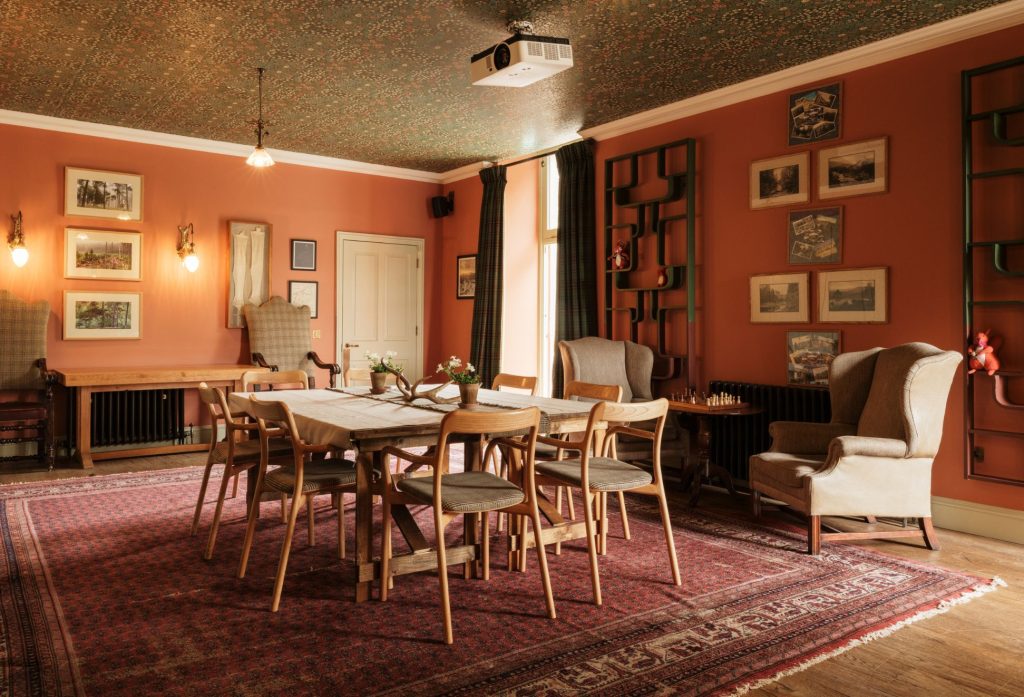 An inviting room with a large wooden table and chairs in the centre and paintings on the orange walls