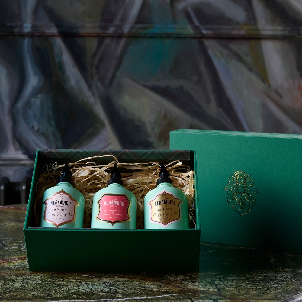 Three Albamhor pastel‑green toiletry products in a green gift box on a bed of shredded brown paper.