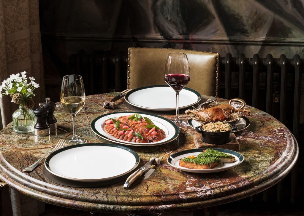 Round dining table set with plated dishes, red and white wine, and place settings in the elegant Clunie Dining Room.