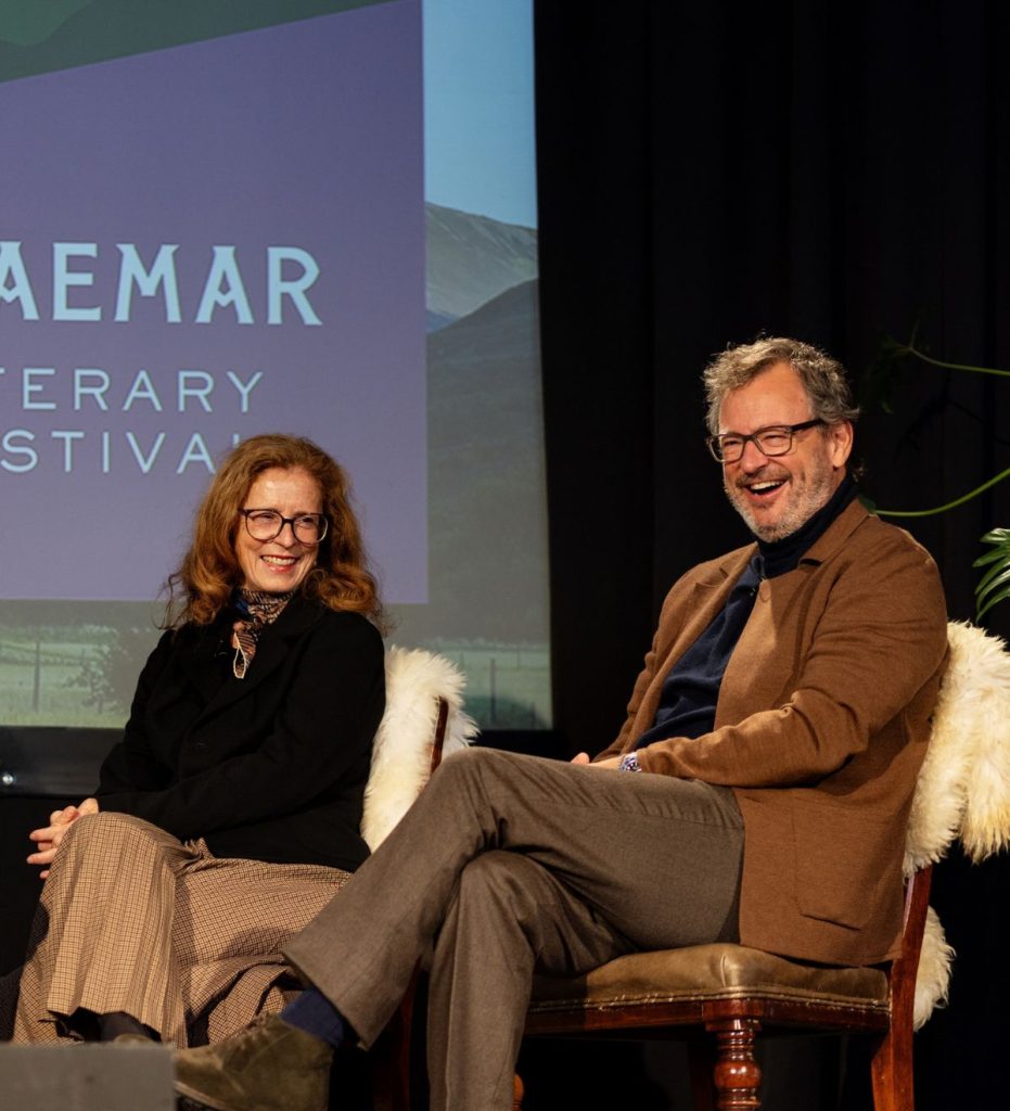 A smiling man and woman seated on stage