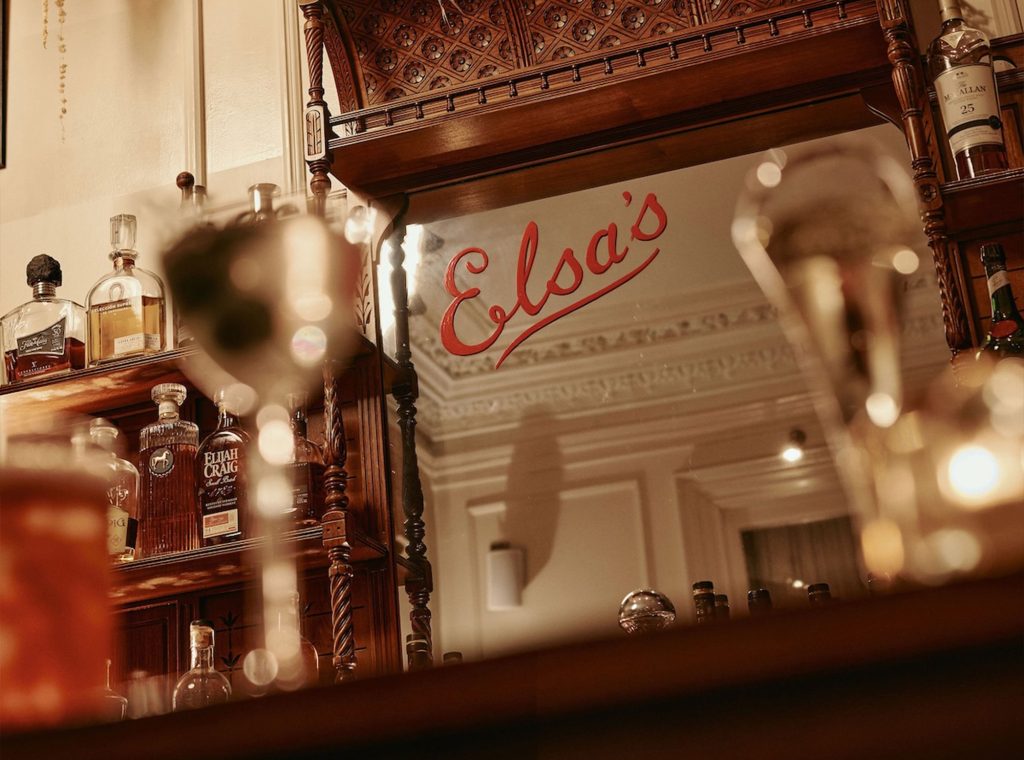 Close-up of Elsa's Cocktail Bar logo on the mirror behind the bar with shelves of spirits either side.