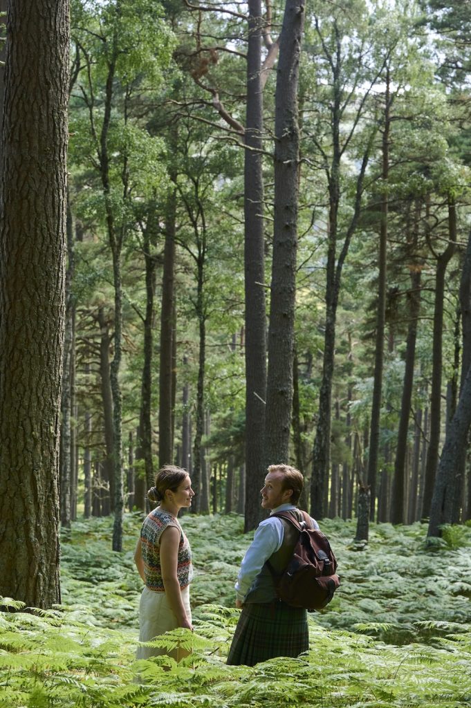Two people in the woods surrounded by tall trees and ferns.