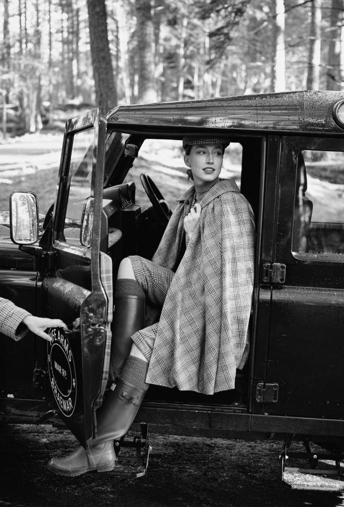 A woman in a tartan cape climbing into a Land Rover.