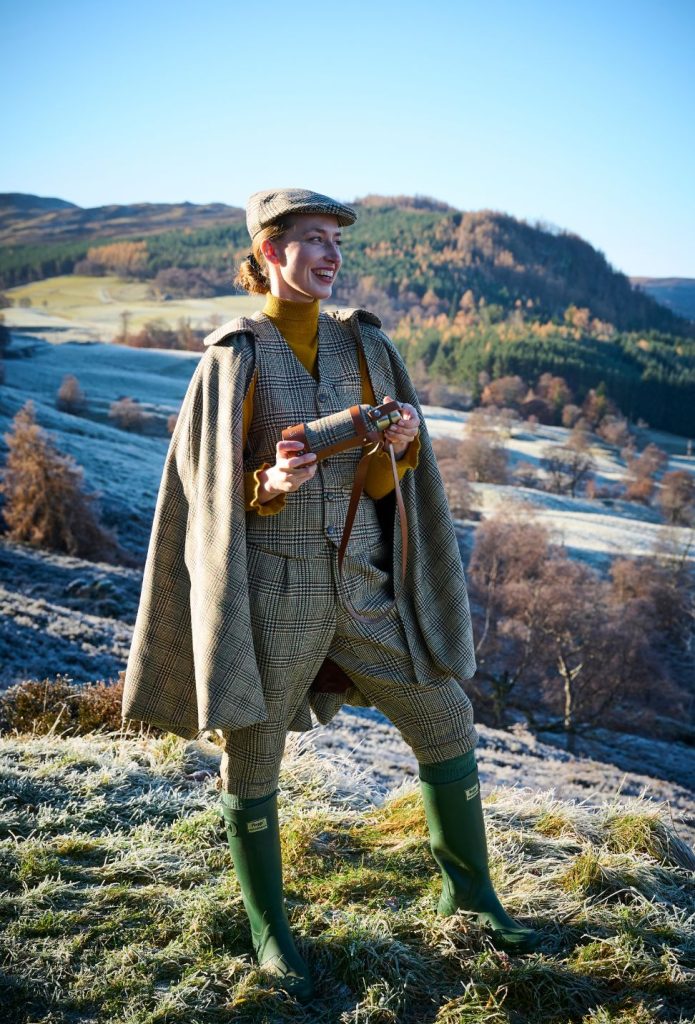 A woman in a tweed cape and hat in a frosty Highland landscape.