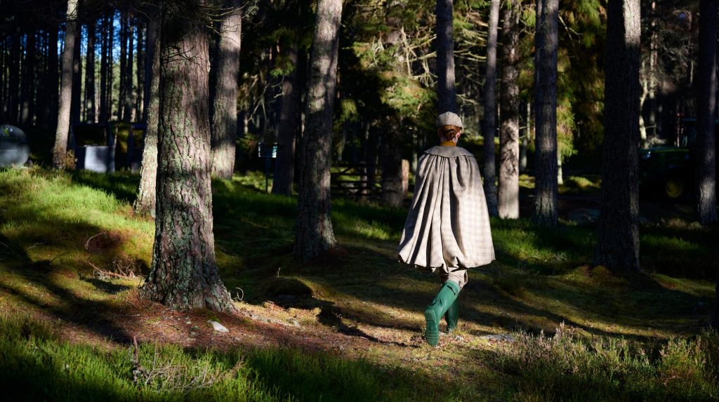 A woman in a tweed cape walking through woodland.