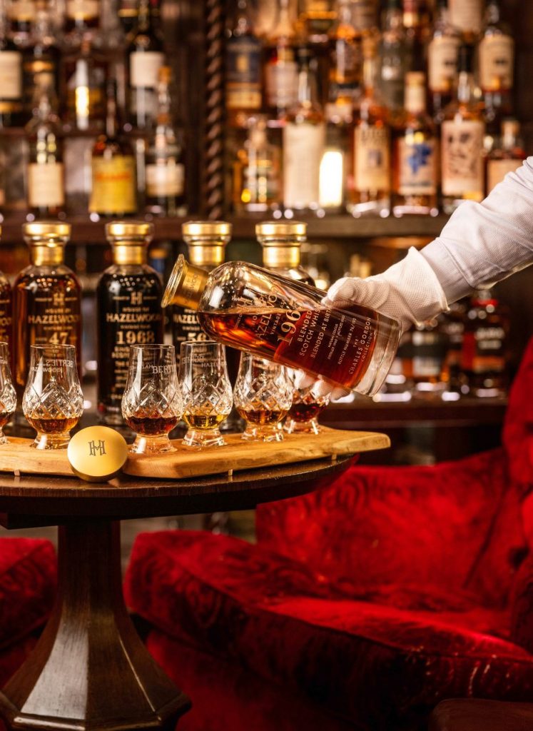 Whisky being poured from a bottle into a flight of tasting glasses.