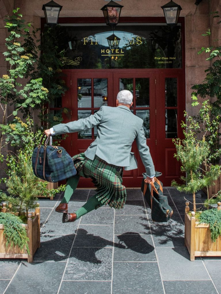 A man jumping with his bags at the front of the hotel