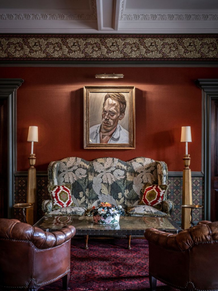 A portrait painting hanging on a red wall above a floral sofa