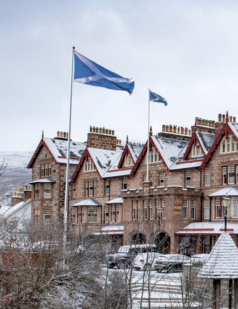 The exterior of the Fife Arms Hotel covered in snow and with the Scottish flag flying above the hotel.