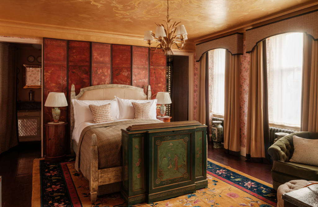Warm, richly decorated Secret Room bedroom featuring a large bed, floral wallpaper, and tall windows with draped curtains.