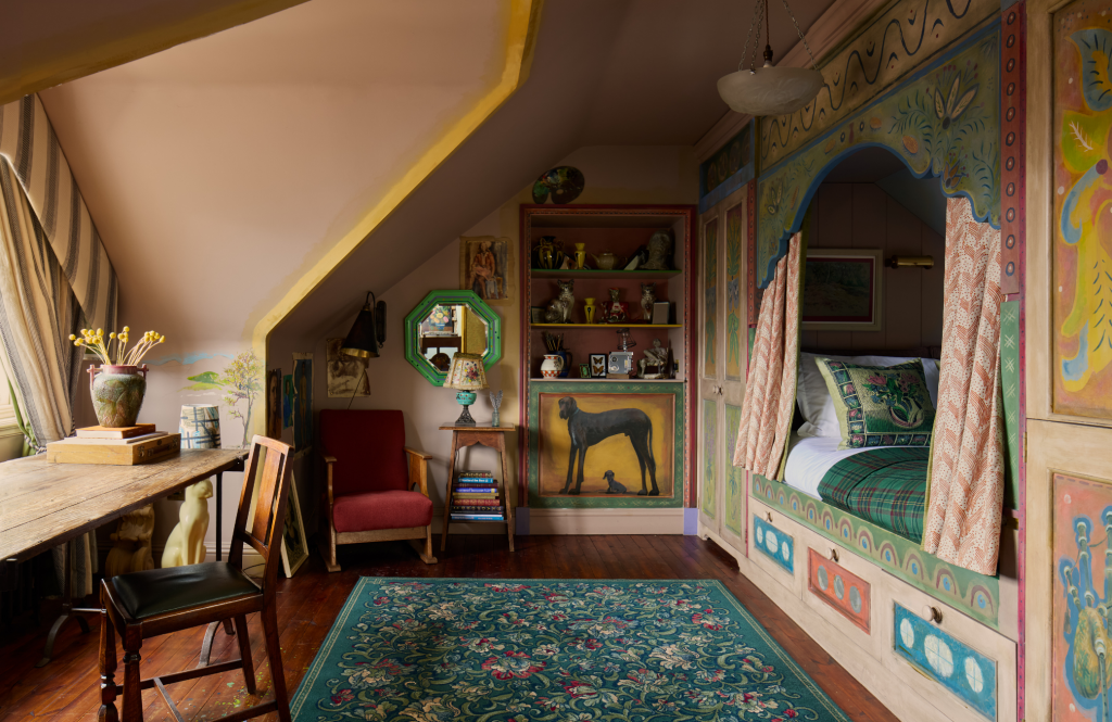 Colourful Artist's Studio room featuring a painted alcove bed, wooden desk, and patterned rug.