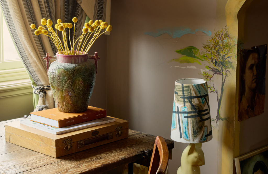 Decorative tabletop arrangement in the Artist's Studio with a textured vase of yellow plants, and a patterned lamp.