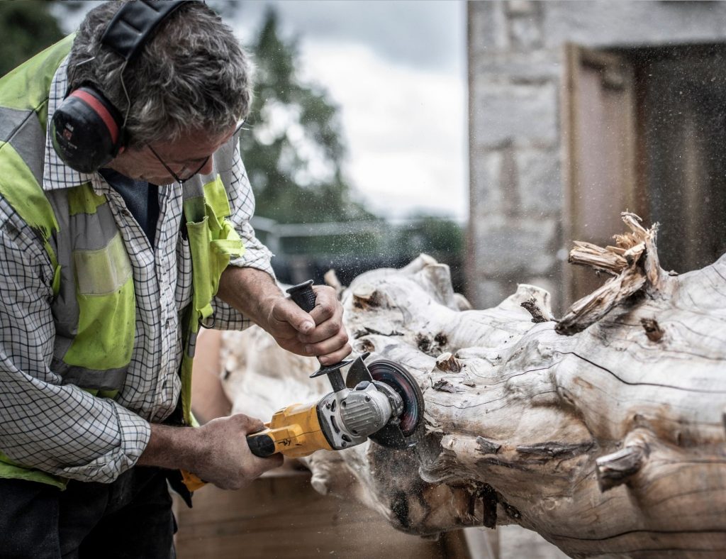 Worker with ear defenders sanding down a tree trunk