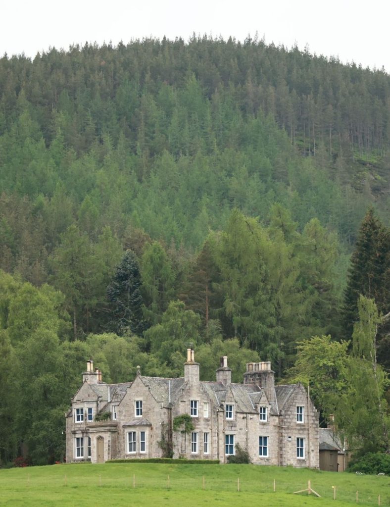 A side view of Balmoral Castle, situated on Balmoral Estate with a hill and trees in the background