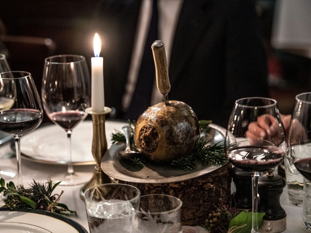 A festive dining table with wine glasses, a lit candle, and a haggis presented with a knife inserted into it for Burns Night.