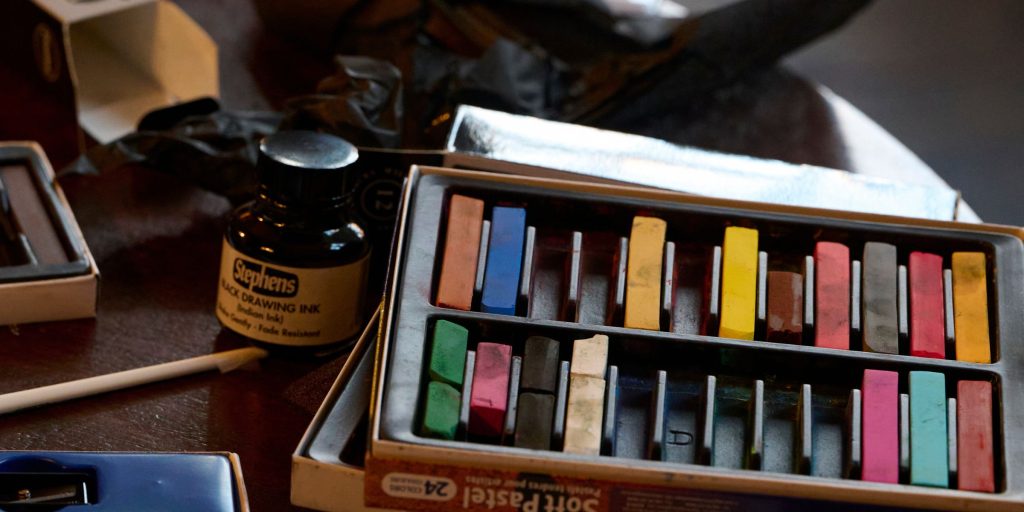 Artist materials on a table including pastels and ink.