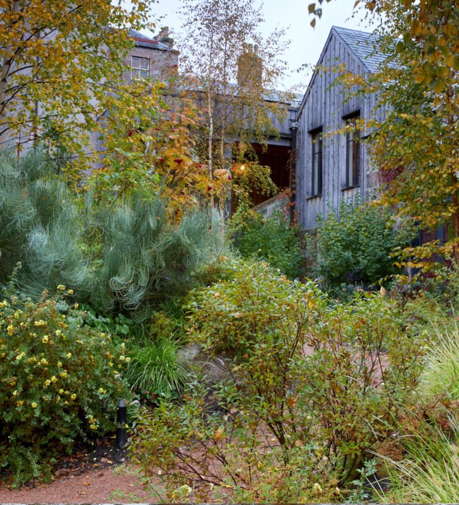 Fife Arms farden filled with shrubs and trees in autumn colours next to a rustic building.