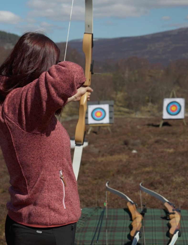 Female guest doing archery with the target in the background.