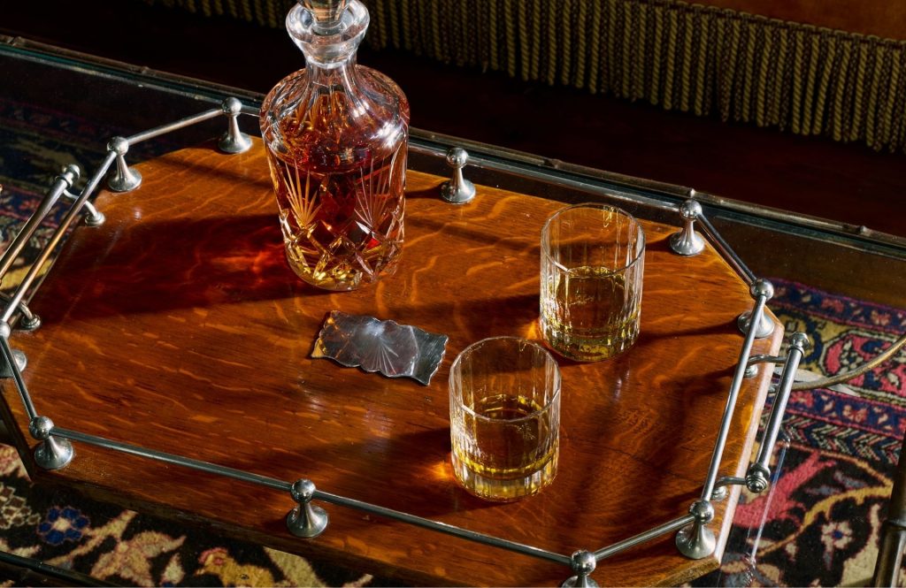 A bottle of whisky and tumblers on a wooden tray.