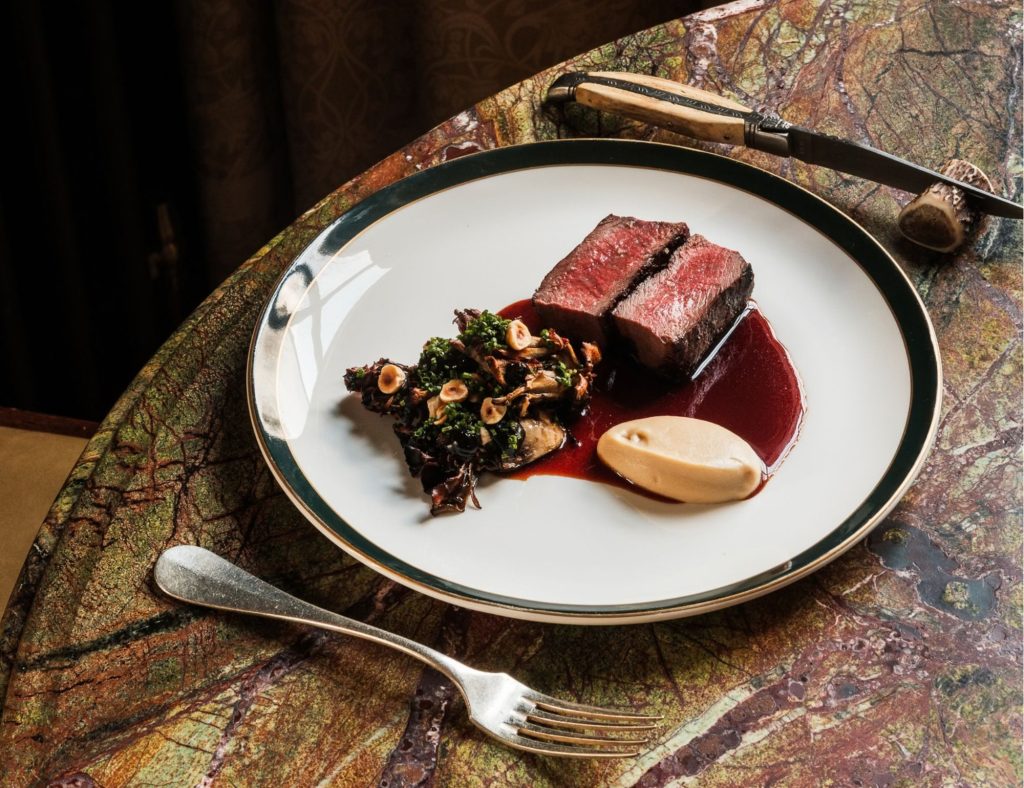 Beef steak cooked medium rare on a white plate at a dining room table with cutlery either side.