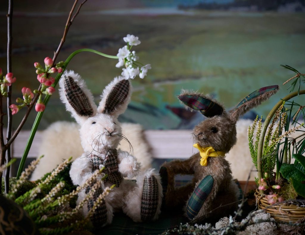 Two stuffed toy hares sat on a table with spring flowers.