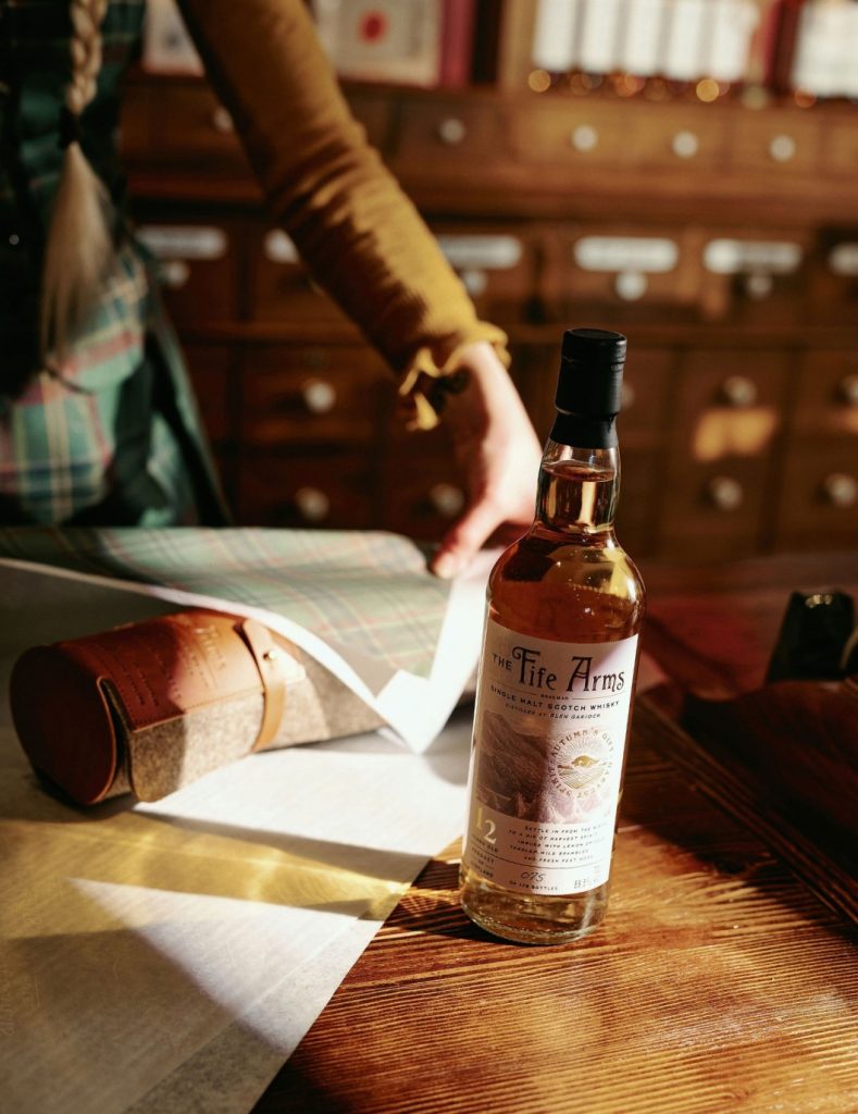 A bottle of Fife Arms Whisky being gift wrapped in tartan paper by a member of the hotel shop team.