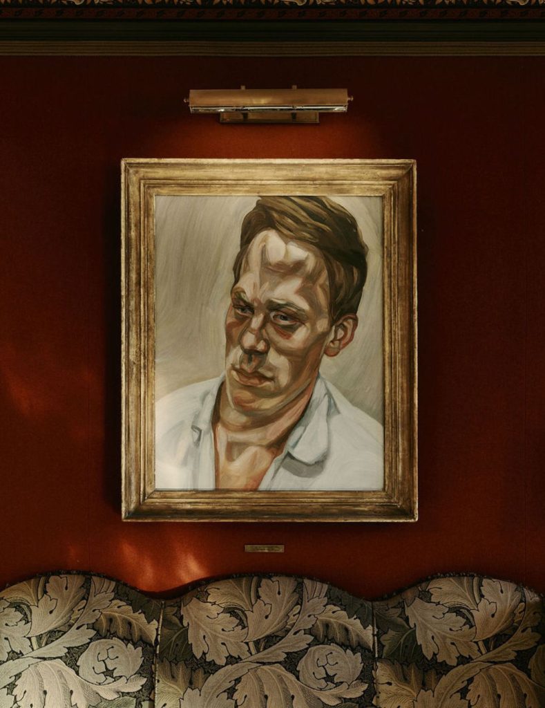 A painting by Lucian Freud hanging on a red wall above a green sofa.