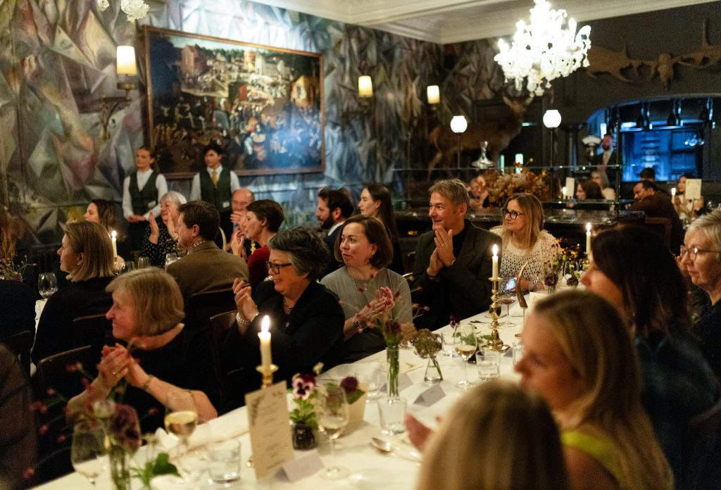 A luxury dinner table setting in The Clunie Dining Room at the Fife Arms, guests are sat either side of two long tables all looking in the same direction.