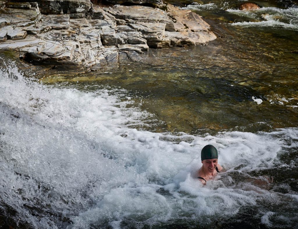 A woman swimming in a Scottish river with a waterfall in the left of the picture.