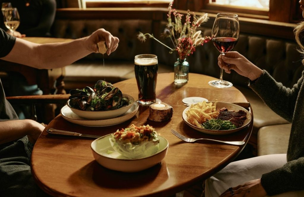 Two people dining at a pub with food and drinks on the table