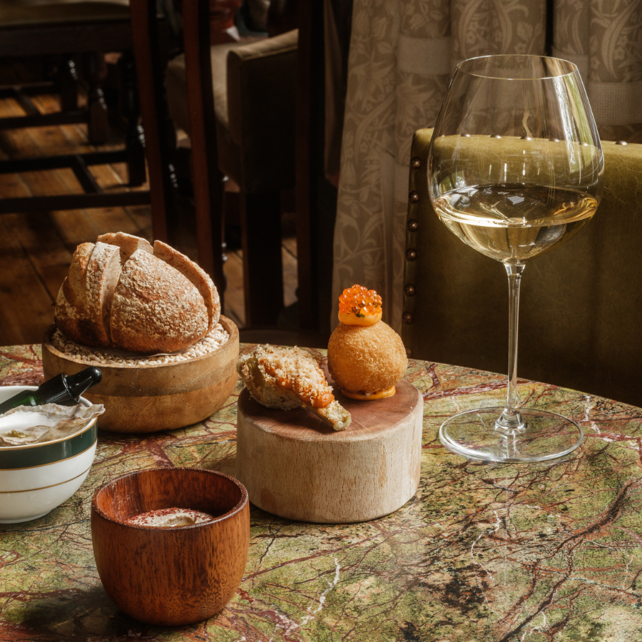 A glass of white wine and snacks on a table in the Clunie Dining Room