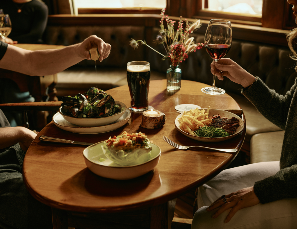 Two people dining at a pub with food and drinks on the table