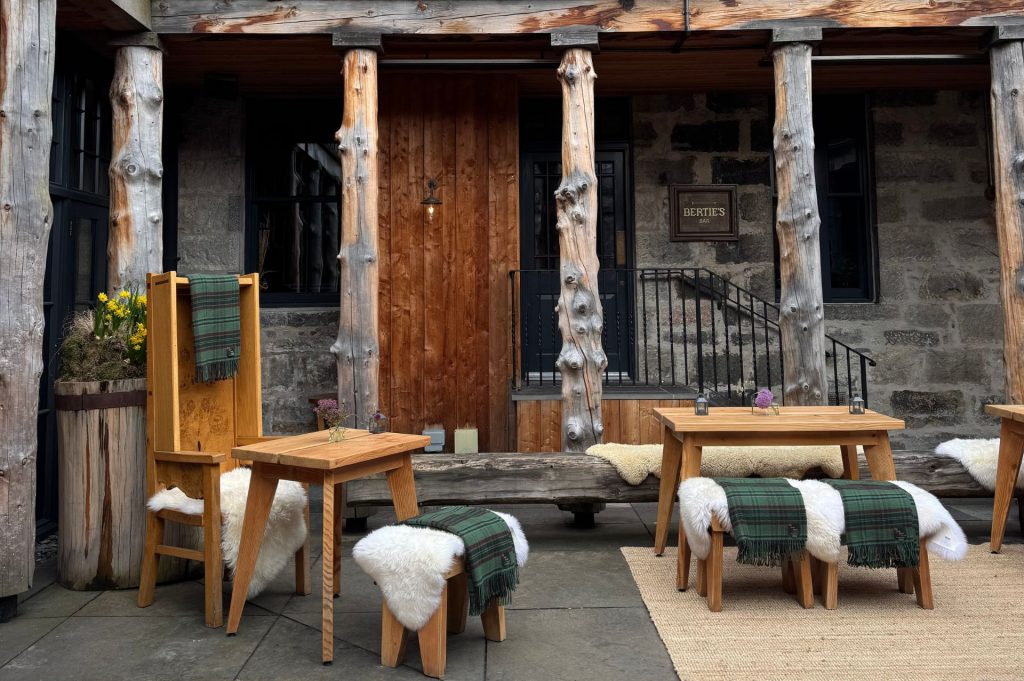 Wooden seating with sheepskins and tartan throws in a courtyard.