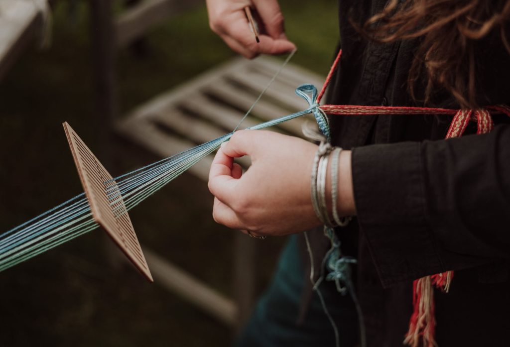Close-up of hands weaving blue thread using a traditional wooden weaving tool.