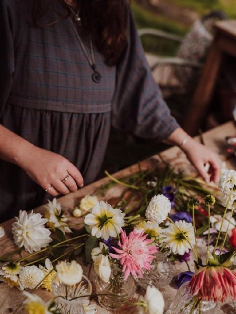Lower half of a lady arranging flowers on a wooden table.