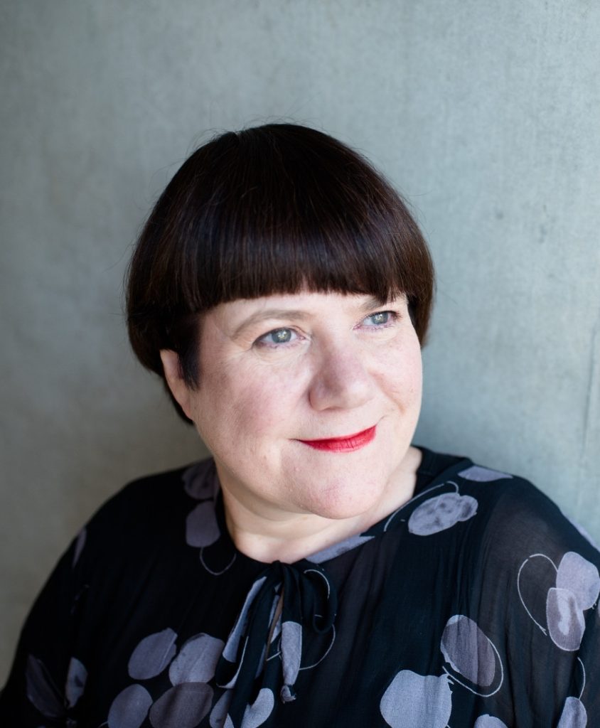 A woman with short dark hair stood in front of a grey background.