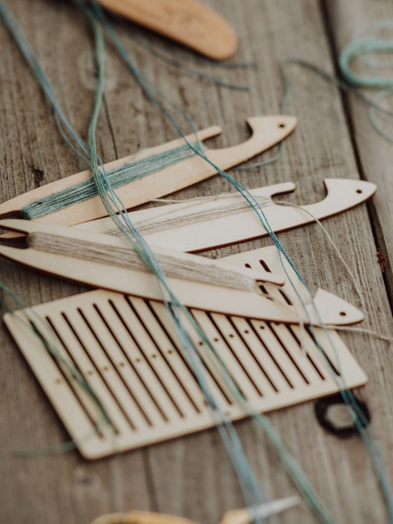 A close-up of traditional wooden weaving tools lying on a table, with blue thread across and within them.