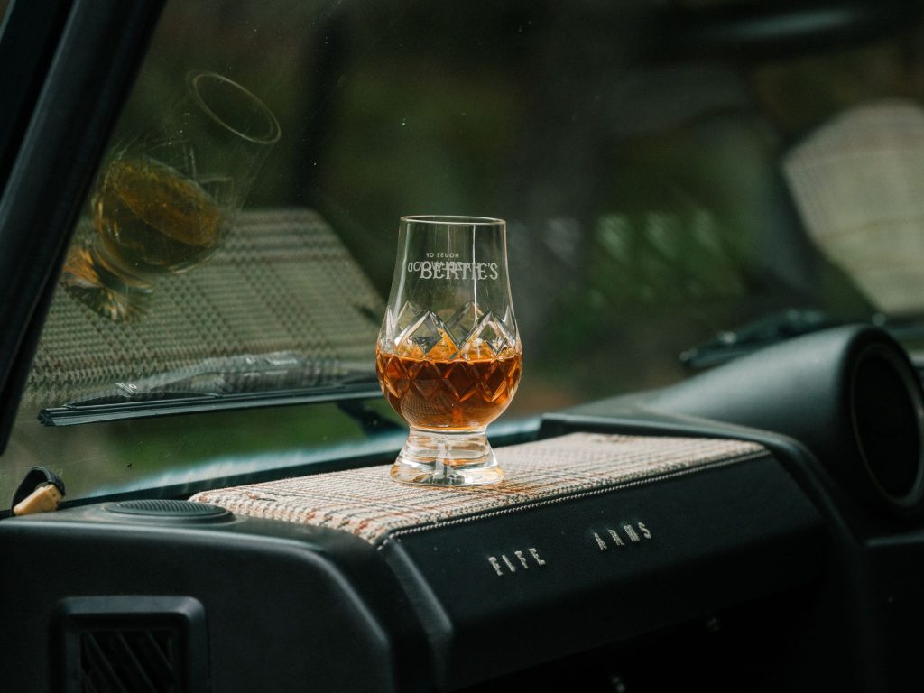 A dram of whisky sat on a tweed dashboard in a Land Rover
