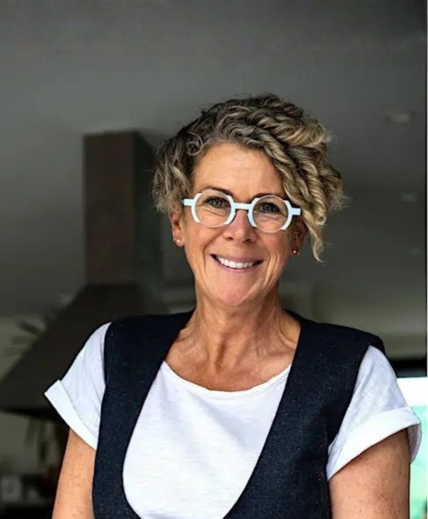 A woman with short curly hair and light blue round glasses