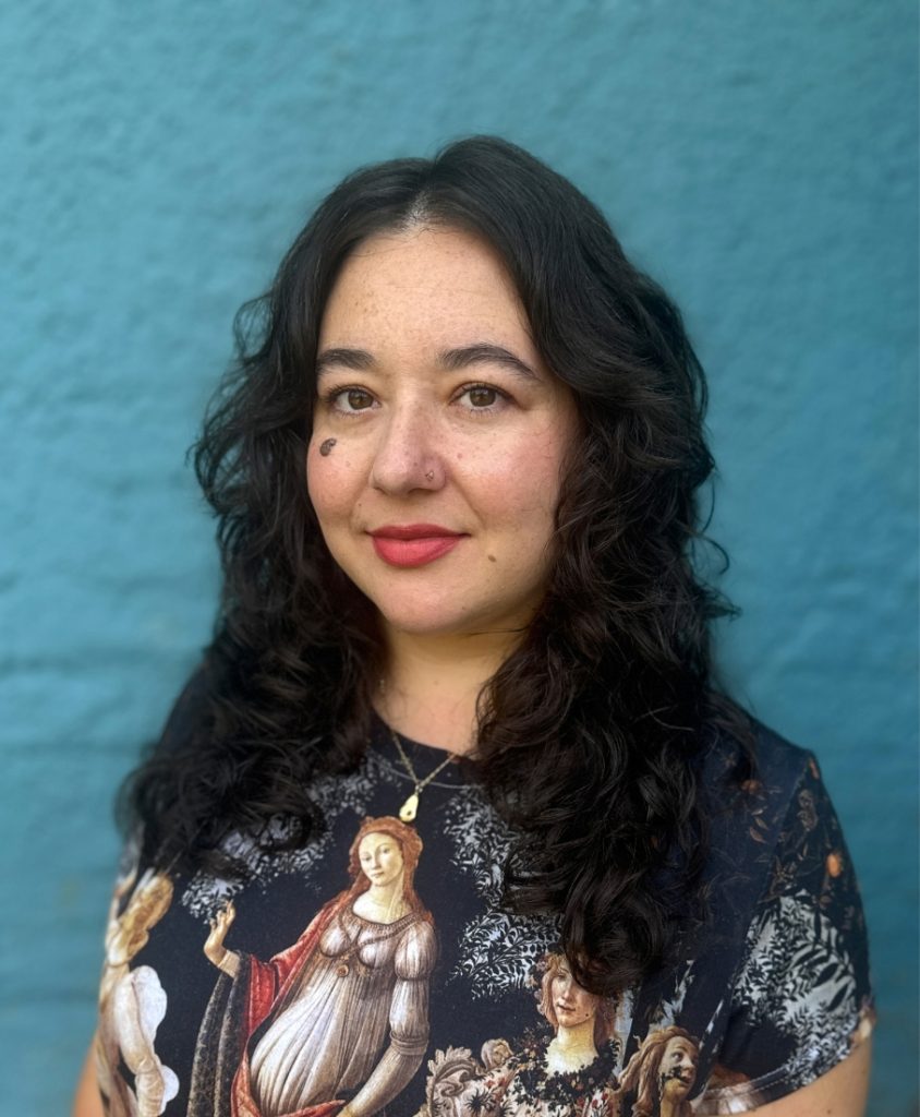 A woman with dark hair stood before a blue wall