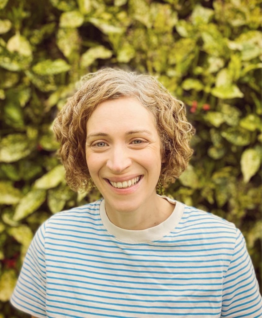 A smiling woman in a stripy top stood before a leafy bush