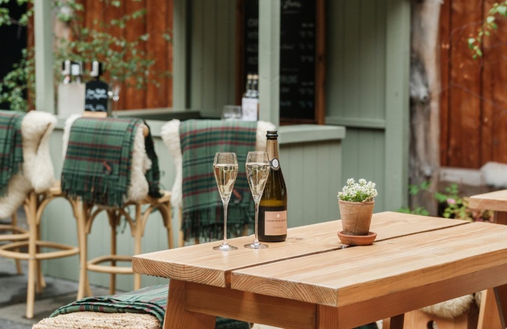 A bottle of champagne and two glasses on a wooden outdoor table
