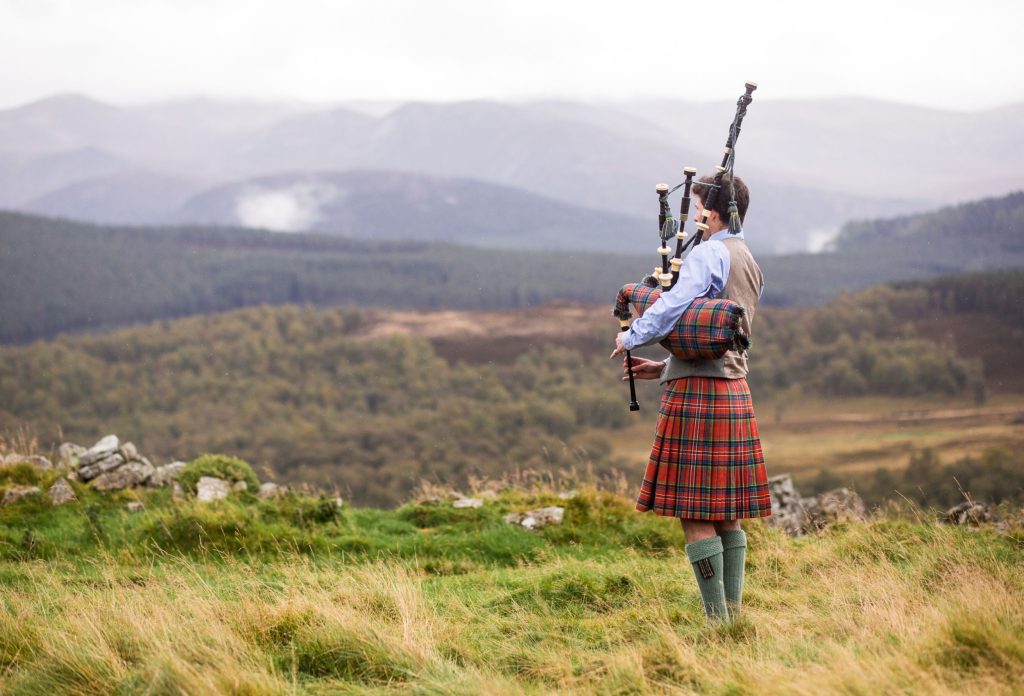 A traditional Scottish bag piper standing on moorland playing the bagpipes.