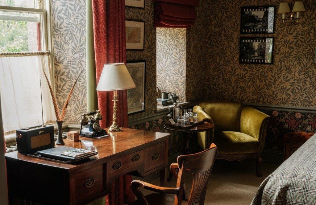 An antique desk and green velvet sofa beside a window